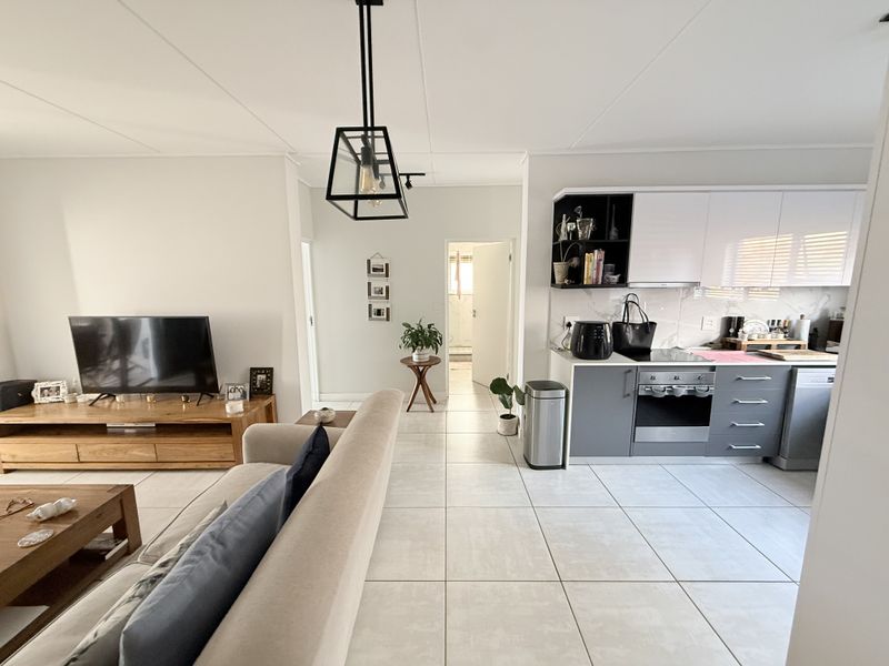Modern open-plan living area featuring a contemporary kitchen with sleek cabinetry, built-in appliances, and neutral tiled flooring throughout the combined space.