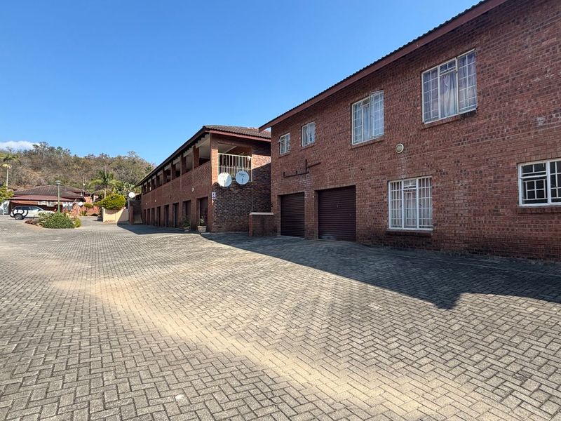 Exterior view of a multi-story face brick apartment complex featuring a paved driveway and integrated garage units.