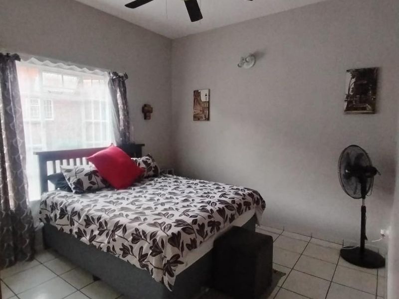 A functional bedroom featuring tiled flooring, a ceiling fan, and a wall-mounted light fixture, providing a simple and practical living space.
