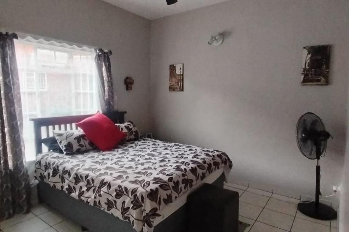 A functional bedroom featuring tiled flooring, a ceiling fan, and a wall-mounted light fixture, providing a simple and practical living space.
