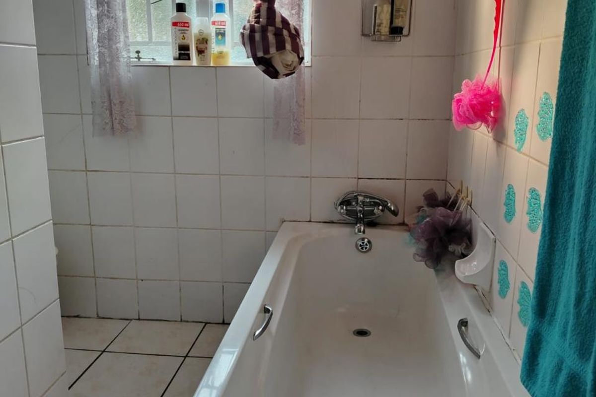 A functional bathroom featuring a standard bathtub with chrome fixtures, tiled walls and flooring, and a window with security bars.