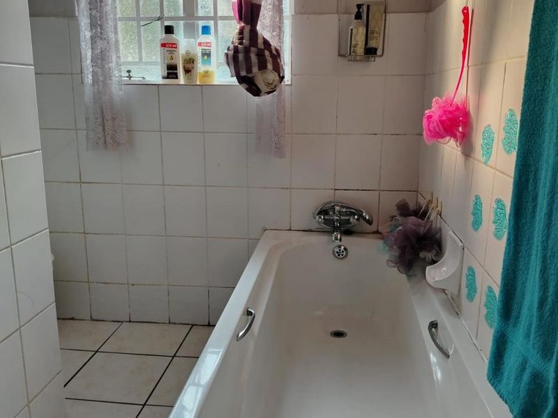 A functional bathroom featuring a standard bathtub with chrome fixtures, tiled walls and flooring, and a window with security bars.