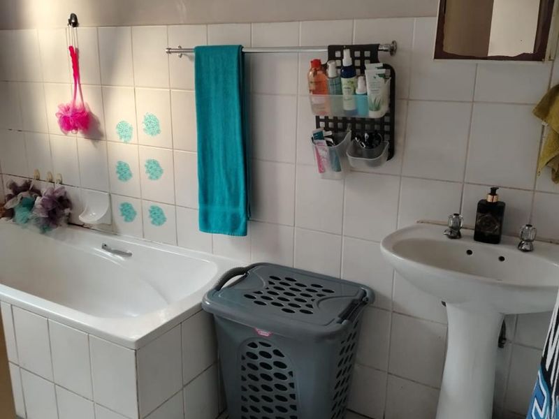 A dated bathroom featuring a pedestal basin and a built-in bathtub with white ceramic wall and floor tiling.