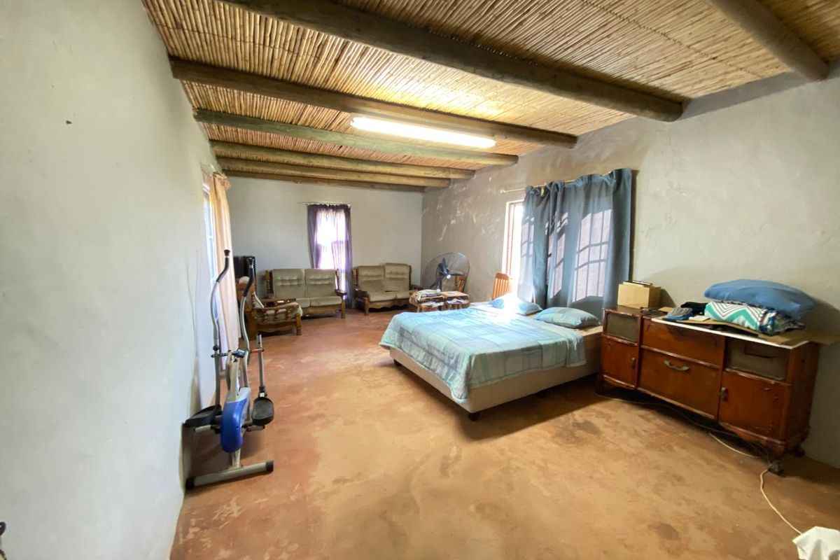 Spacious bedroom featuring a rustic reed ceiling with exposed timber beams and a concrete floor, offering a blank canvas for renovation.