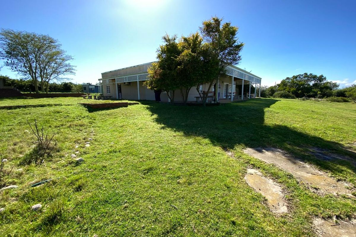Rear view of the farm dwelling featuring a covered veranda with lattice detailing, set within a large, open grassed area.
