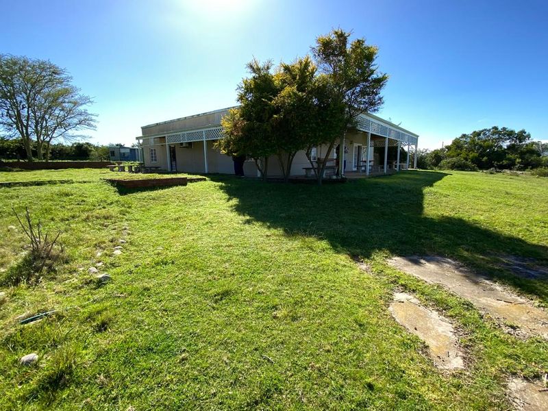 Rear view of the farm dwelling featuring a covered veranda with lattice detailing, set within a large, open grassed area.