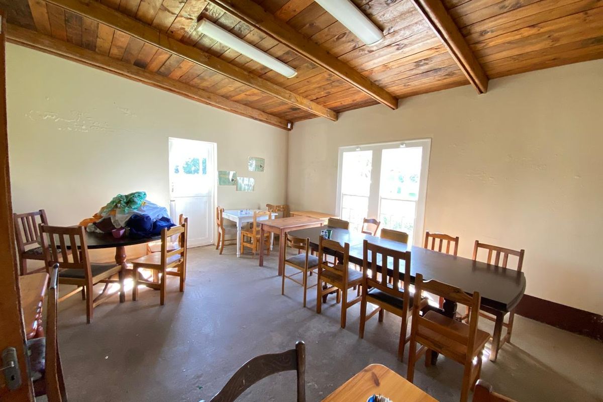 Spacious living area featuring exposed timber beam ceilings, concrete flooring, and ample natural light through multiple windows.