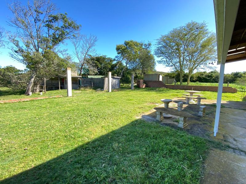 Spacious rear garden area featuring a concrete patio, structural support columns, and an outbuilding, set within a rural farm property landscape.