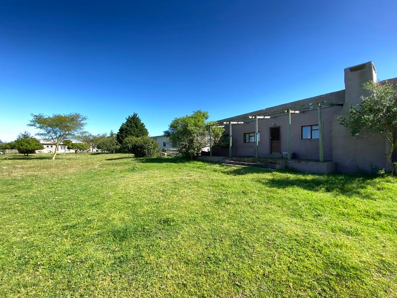 Rear view of the farm property featuring a large lawn, a masonry chimney, and a timber pergola structure attached to the building.