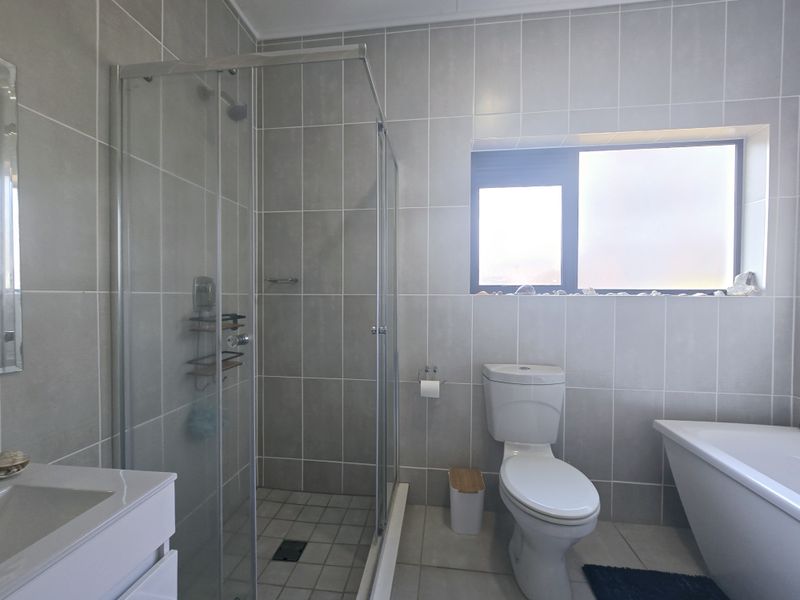 Modern bathroom featuring a glass-enclosed shower, a bathtub, a toilet, and a vanity basin, finished with neutral wall and floor tiles.