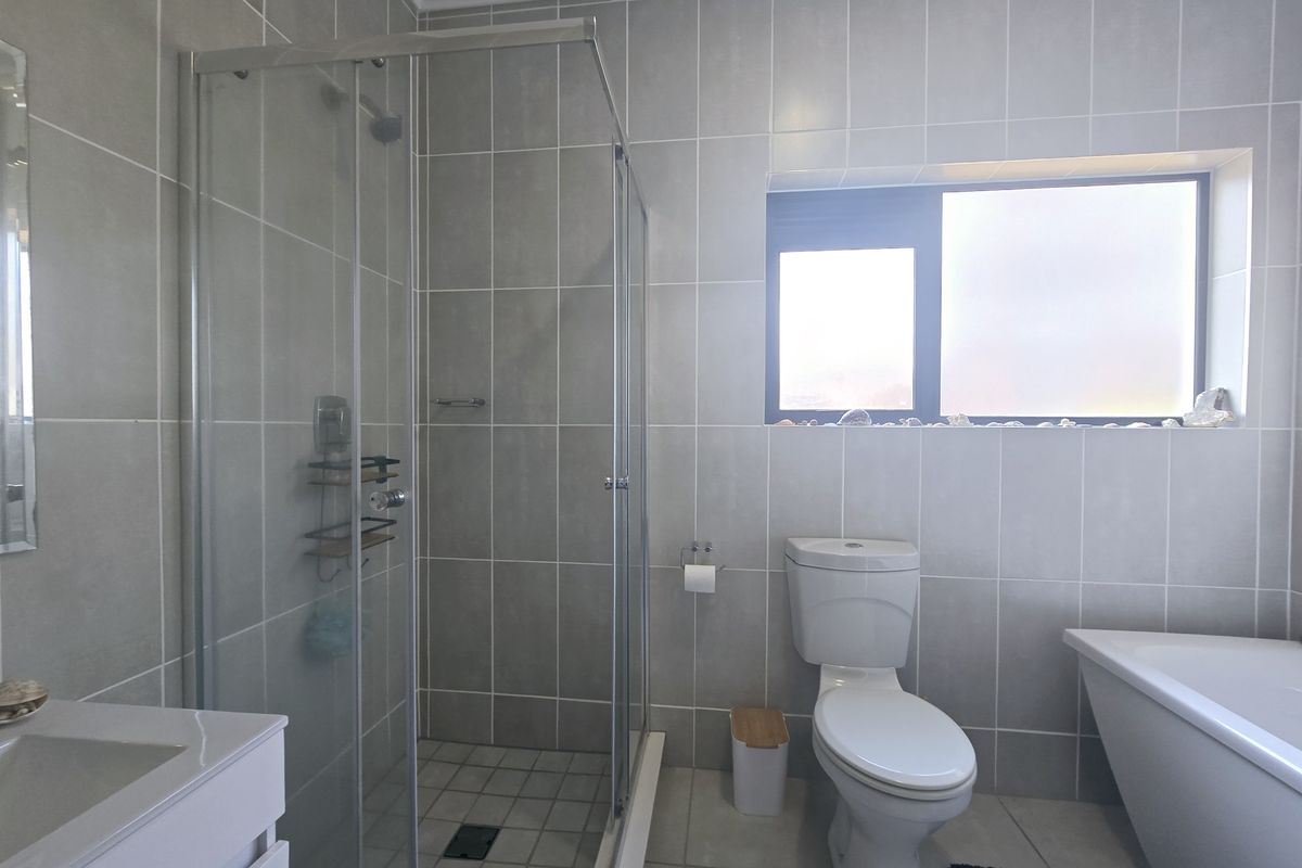 Modern bathroom featuring a glass-enclosed shower, a bathtub, a toilet, and a vanity basin, finished with neutral wall and floor tiles.