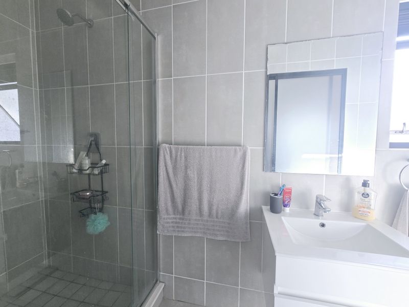 A modern bathroom featuring a glass-enclosed shower, a vanity basin with a mixer tap, and neutral grey wall tiling.