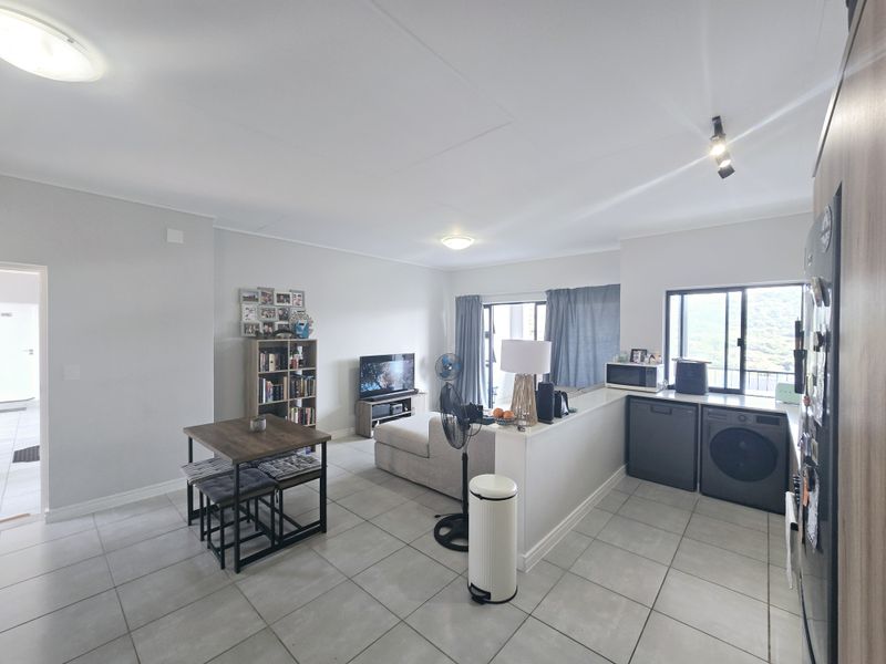 Open-plan living and kitchen area featuring neutral tiled flooring, a functional kitchen island, and direct access to an outdoor balcony through sliding glass doors.