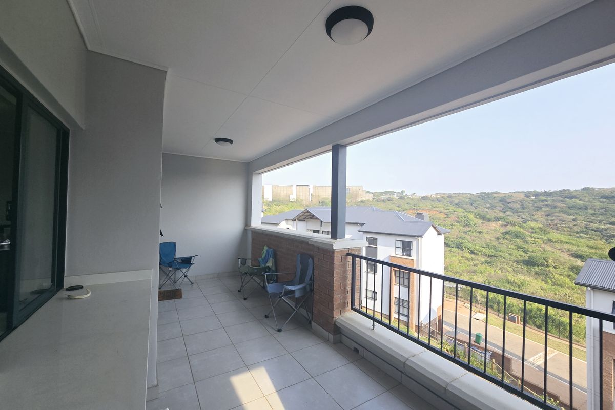 A spacious covered balcony featuring tiled flooring, a brick accent wall, and a metal balustrade, offering scenic views of the surrounding landscape.