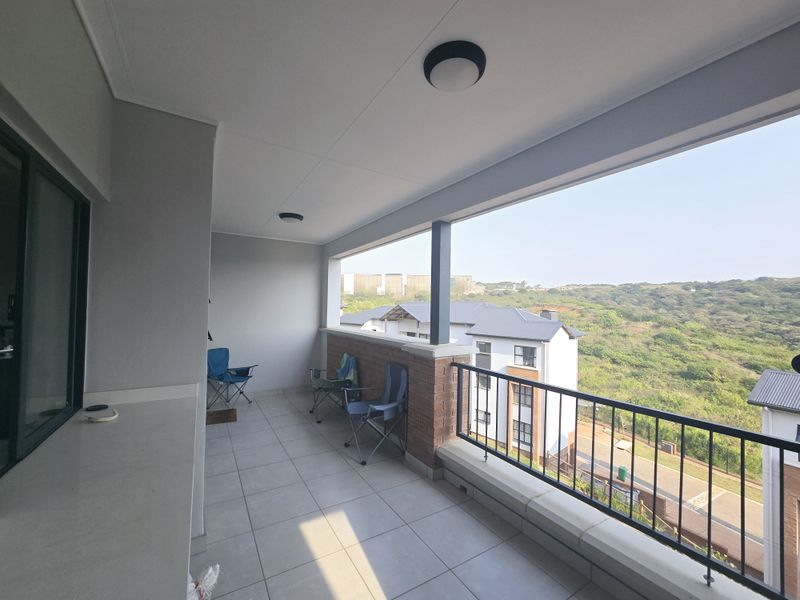 A spacious covered balcony featuring tiled flooring, a brick accent wall, and a metal balustrade, offering scenic views of the surrounding landscape.