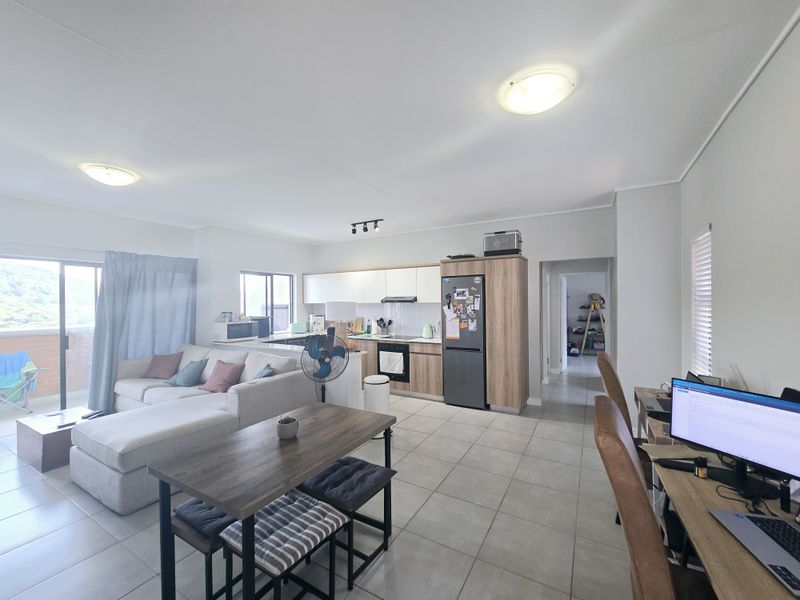 Spacious open-plan living area featuring a modern kitchen with built-in cabinetry, tiled flooring, and direct access to a balcony through sliding glass doors.