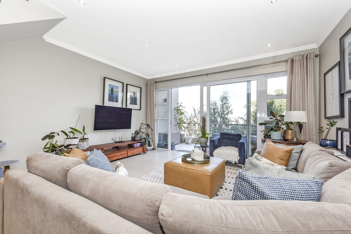 A bright and spacious living room featuring large sliding glass doors that open onto a private balcony, complemented by neutral tiled flooring and recessed lighting.