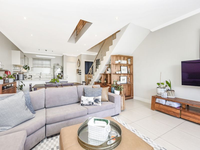 An open-plan living and kitchen area featuring tiled floors, a modern staircase, recessed lighting, and a functional kitchen with integrated cabinetry.