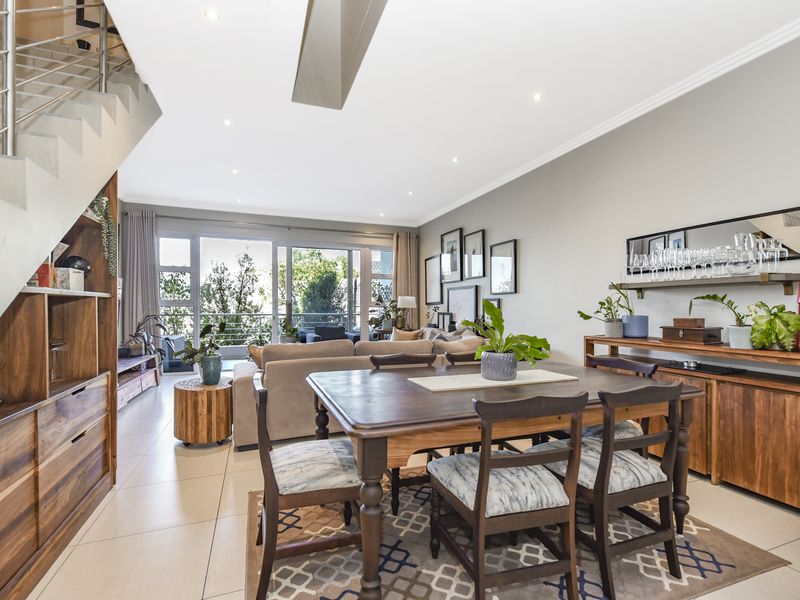 Spacious open-plan living and dining area featuring tiled floors, recessed lighting, and a modern staircase, with large sliding doors leading to an outdoor space.