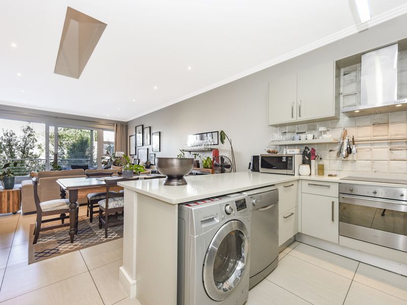 Modern open-plan living area featuring a well-equipped kitchen with stone countertops, integrated appliances, and seamless flow to a bright balcony through sliding glass doors.