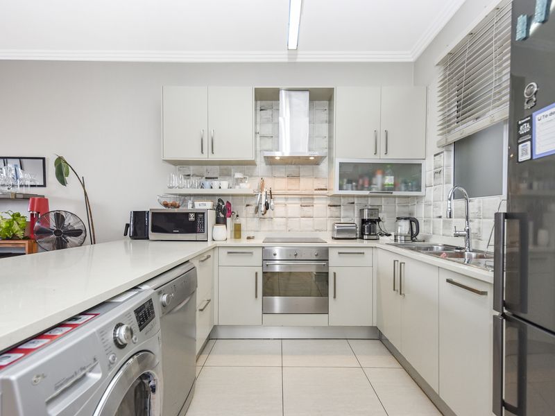 Modern U-shaped kitchen featuring light-toned cabinetry, stone countertops, integrated appliances, tiled backsplash, and convenient laundry plumbing connections.