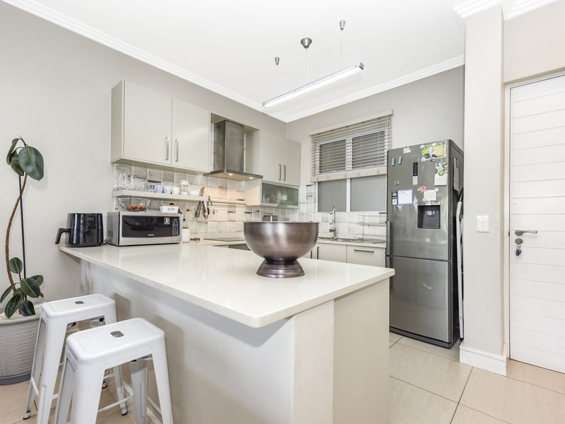 Modern kitchen featuring quartz countertops, ample built-in cabinetry, a stainless steel extractor fan, and a tiled backsplash with neutral finishes.