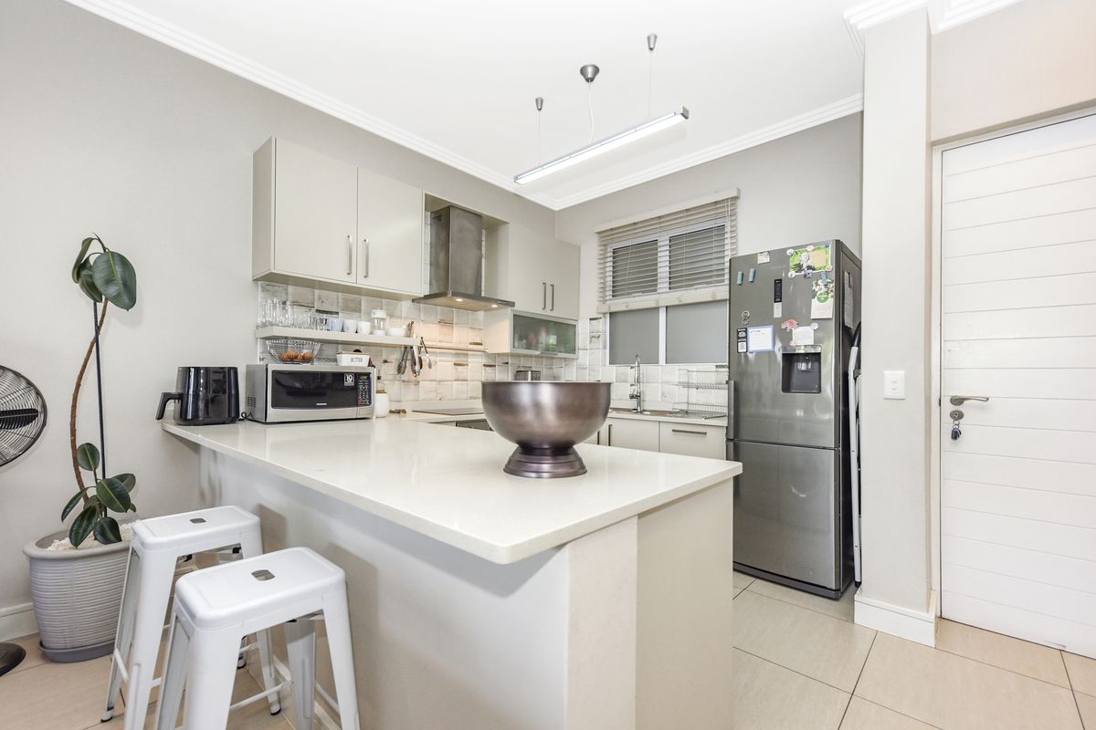 Modern kitchen featuring quartz countertops, ample built-in cabinetry, a stainless steel extractor fan, and a tiled backsplash with neutral finishes.