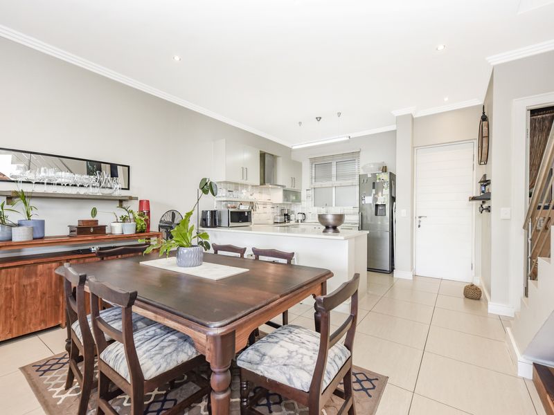 An open-plan living and dining area featuring a modern kitchen with stone countertops, tiled flooring, and a staircase leading to the upper level.