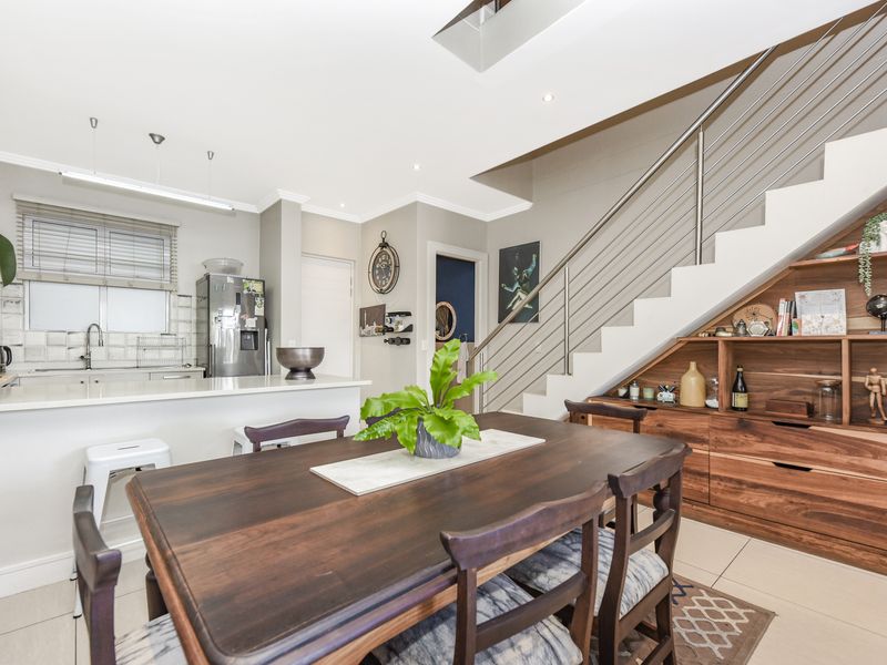 Open-plan living and dining area featuring a modern kitchen with stone countertops and a staircase with a sleek stainless steel balustrade.