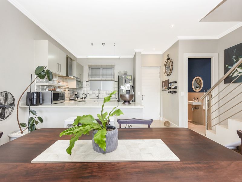 Open plan kitchen and dining area featuring modern cabinetry, stone countertops, and a staircase with a contemporary metal balustrade leading to the upper level.