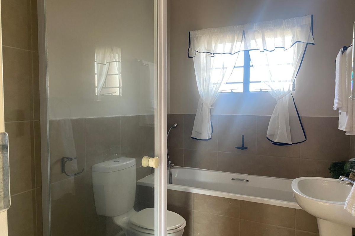 A functional bathroom featuring a shower enclosure, bathtub, pedestal basin, and neutral wall tiling, offering a clean and practical layout.