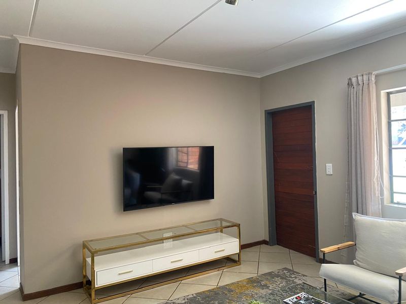 A well-maintained living room featuring neutral wall tones, tiled flooring, and a solid wooden door.