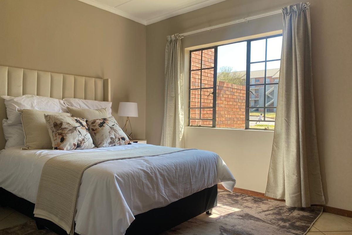 A well-lit bedroom featuring tiled flooring, a steel-framed window, and neutral wall finishes, providing a comfortable and functional living space.
