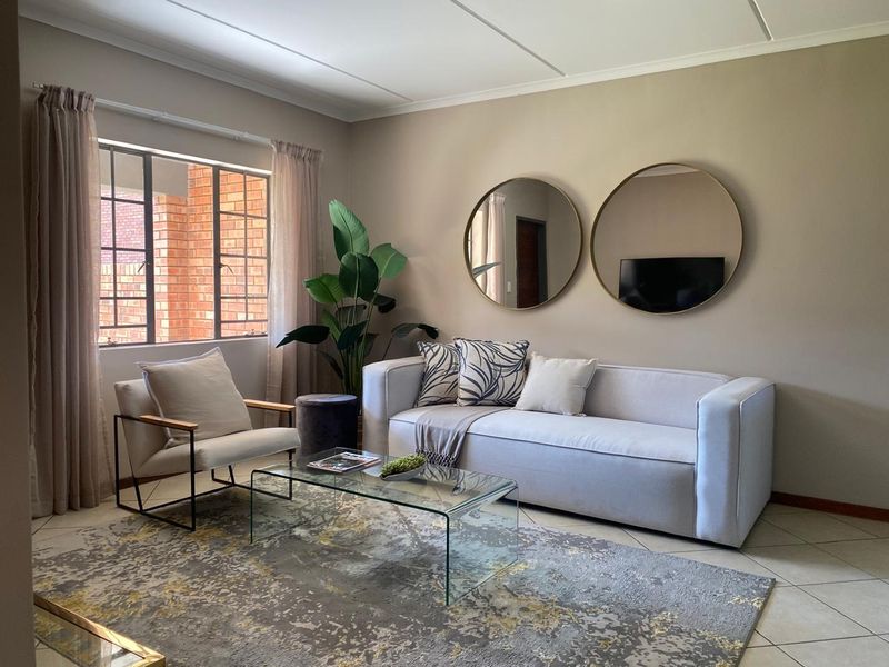A well-maintained living room featuring neutral wall tones, tiled flooring, and a large steel-framed window providing natural light.
