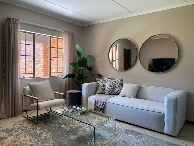 A well-maintained living room featuring neutral wall tones, tiled flooring, and a large steel-framed window providing natural light.