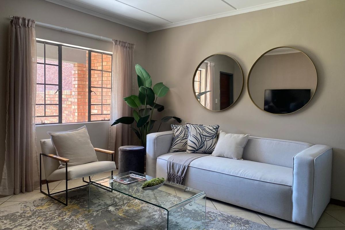 A well-maintained living room featuring neutral wall tones, tiled flooring, and a large steel-framed window providing natural light.