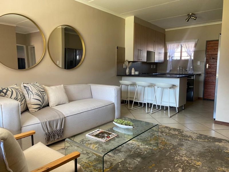 An open-plan living area featuring a modern kitchen with built-in cabinetry, stone countertops, and a breakfast bar, seamlessly connected to the lounge space.