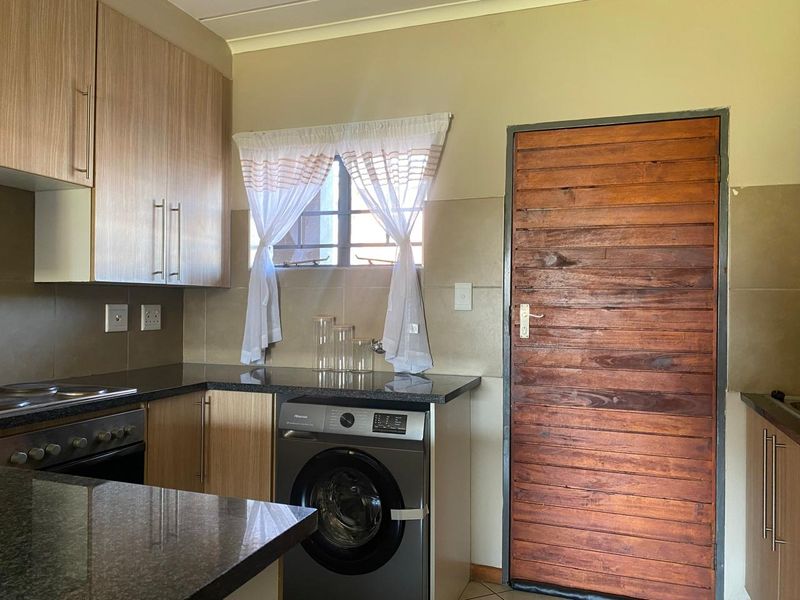 A functional kitchen featuring laminate cabinetry, granite countertops, a built-in oven, and a hob, with a solid timber door leading to the exterior.