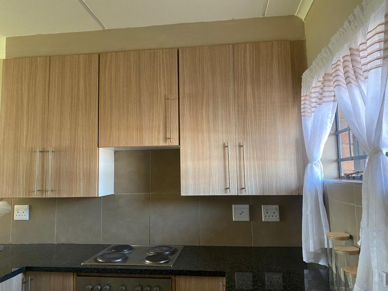 A functional kitchen featuring light wood-grain cabinetry, dark granite countertops, a built-in electric hob and oven, and a tiled backsplash.