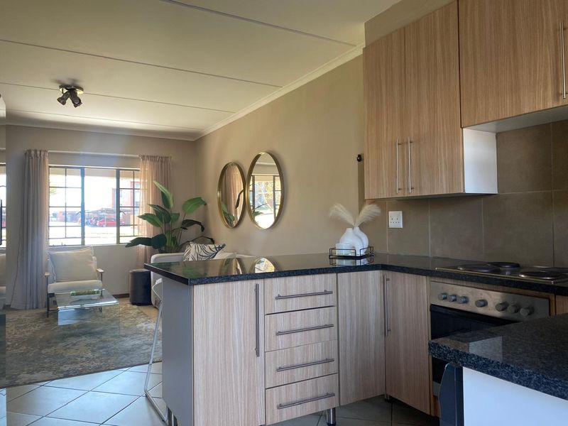 Open-plan living area featuring a modern kitchen with wood-finish cabinetry, granite countertops, and integrated appliances, flowing into a bright, comfortable lounge space.