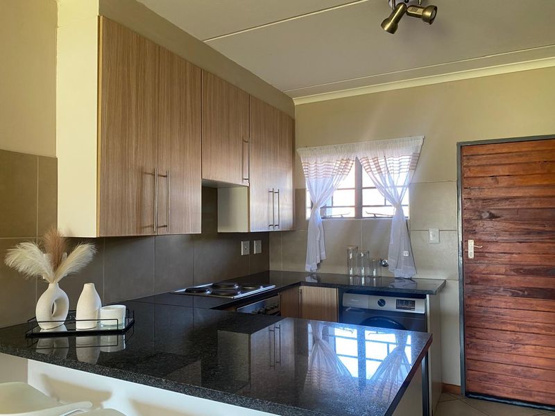 A functional kitchen featuring wood-finish cabinetry, dark granite countertops, a built-in hob and oven, and a tiled backsplash.