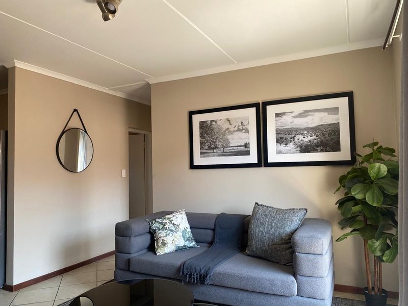 A well-maintained living room featuring neutral wall tones, tiled flooring, and modern ceiling spotlighting, creating a comfortable and inviting atmosphere.