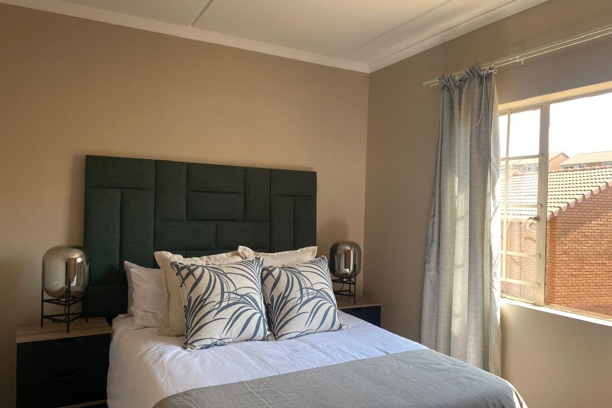 A well-lit bedroom featuring neutral wall tones, coving, and a window with a curtain rail, providing a comfortable and functional living space.