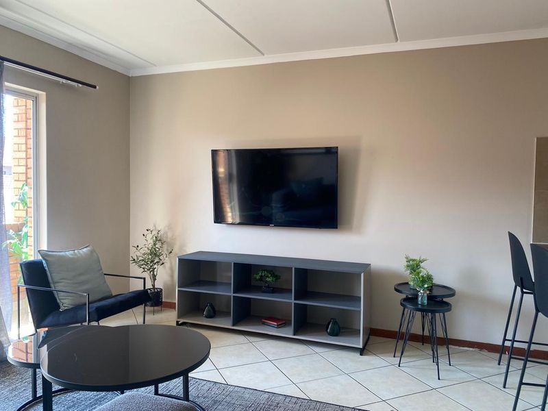 A well-maintained living room featuring neutral wall tones, tiled flooring, and a sliding glass door providing natural light.