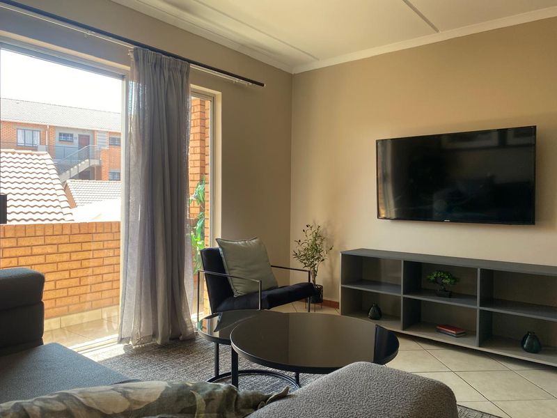 A well-maintained living room featuring tiled floors, neutral wall tones, and a large sliding glass door providing access to an outdoor balcony area.