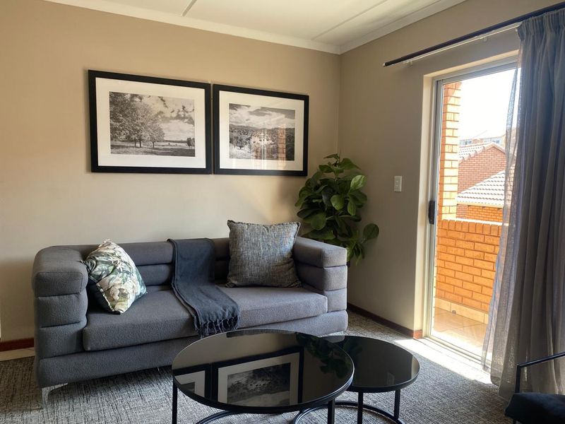 A comfortable living room featuring neutral walls, carpeted flooring, and a sliding glass door providing access to an outdoor balcony area.