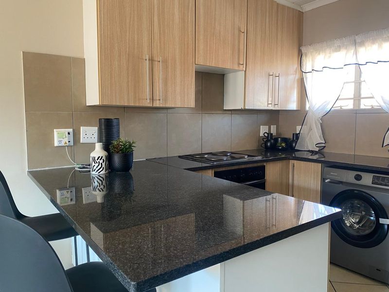 Modern kitchen featuring granite countertops, light wood-finish cabinetry, built-in electric hob and oven, and an integrated washing machine.