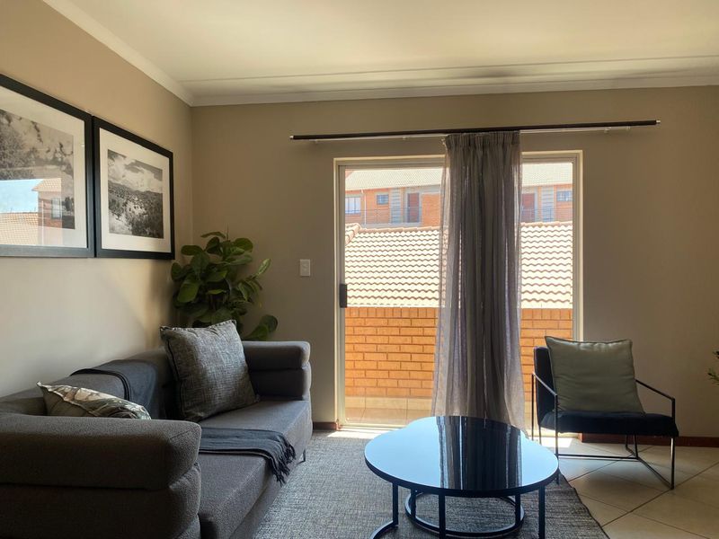 A well-lit living room featuring tiled flooring, coved ceilings, and a sliding glass door providing access to an outdoor balcony area.