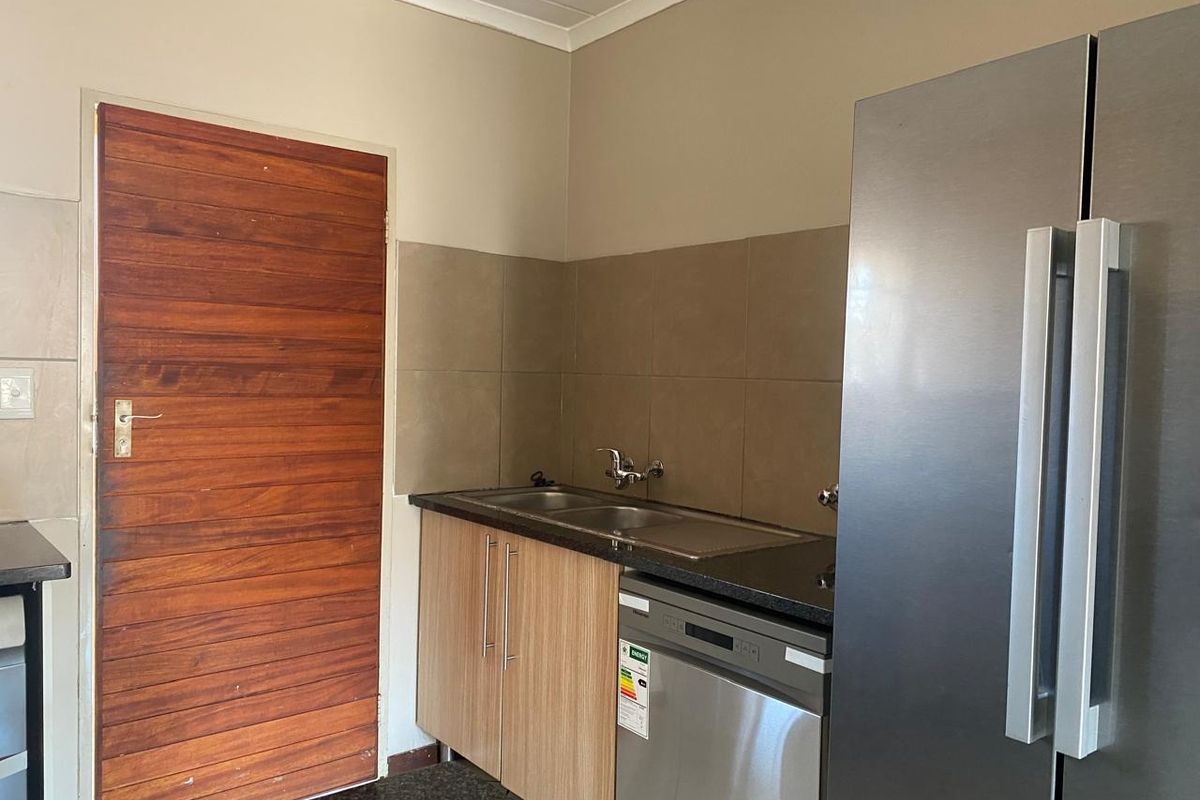 A functional kitchen area featuring a double sink, tiled backsplash, granite countertops, and modern laminate cabinetry.