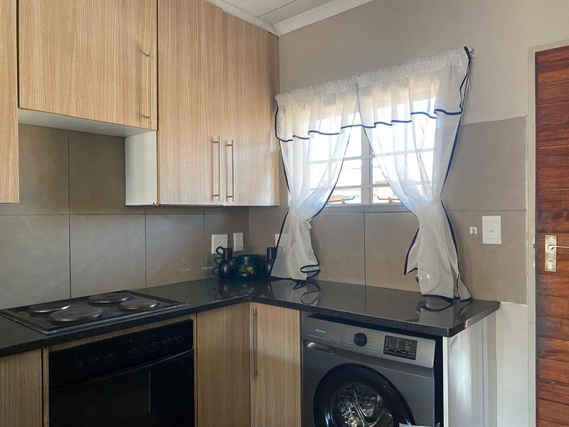 A functional kitchen featuring light wood-finish cabinetry, dark granite countertops, a built-in electric hob and oven, and a tiled backsplash.